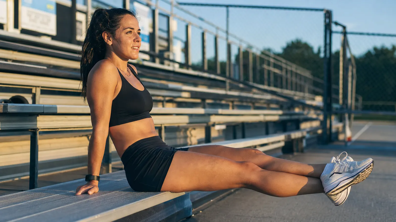 Athlete sitting on a gym bench wearing full-leg pneumatic compression boots connected to a portable control unit