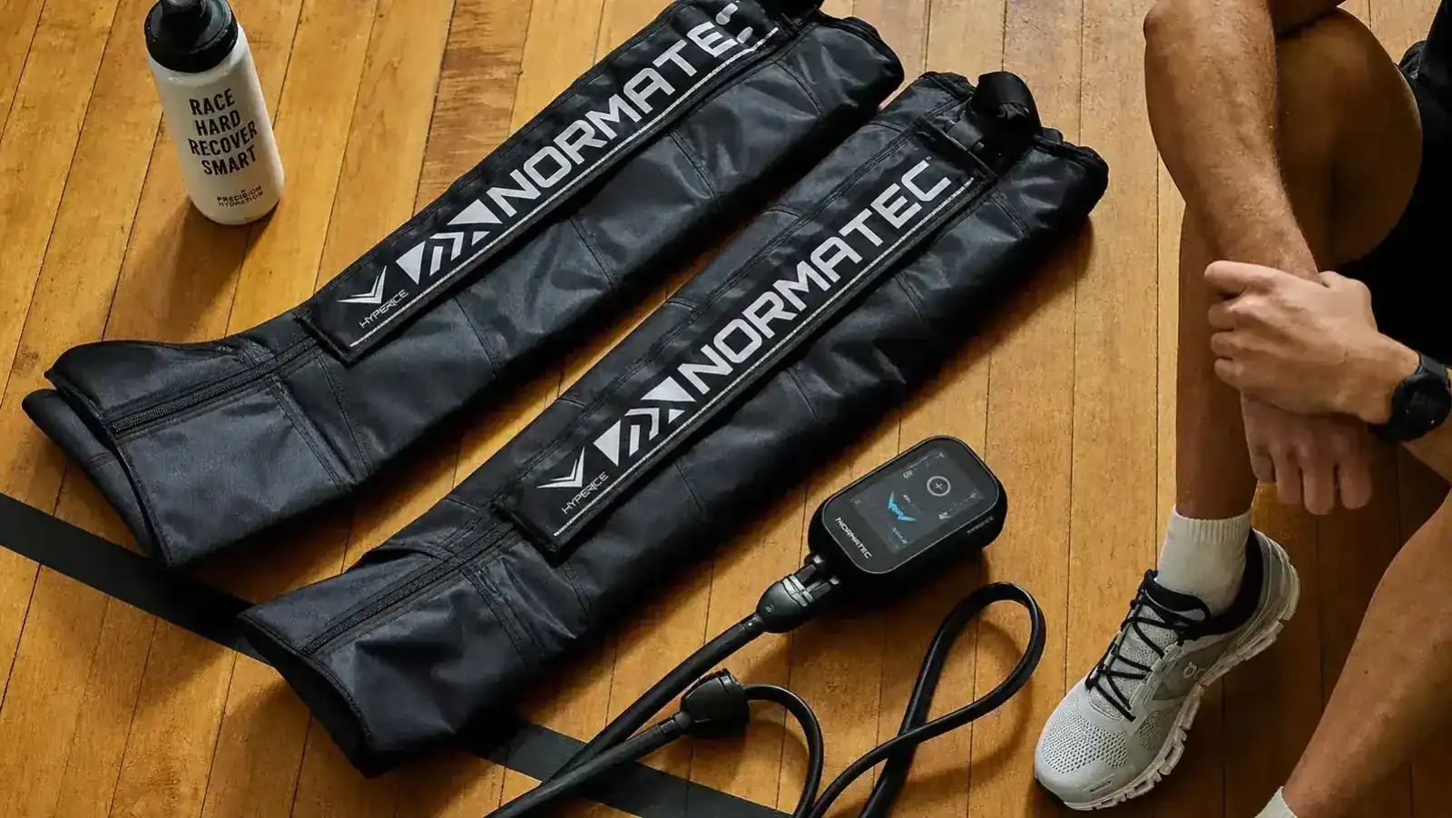 Person sitting on a gym bench with QUINEAR compression boots inflated around both legs after a workout