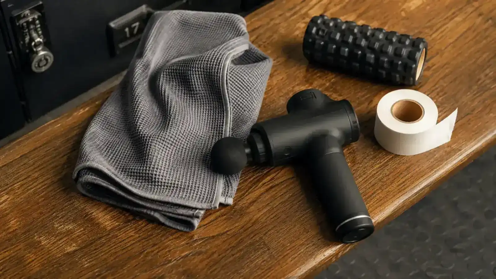 Theragun Relief massage gun resting on a gym bag next to foam roller and water bottle, overhead flat-lay on slate surface