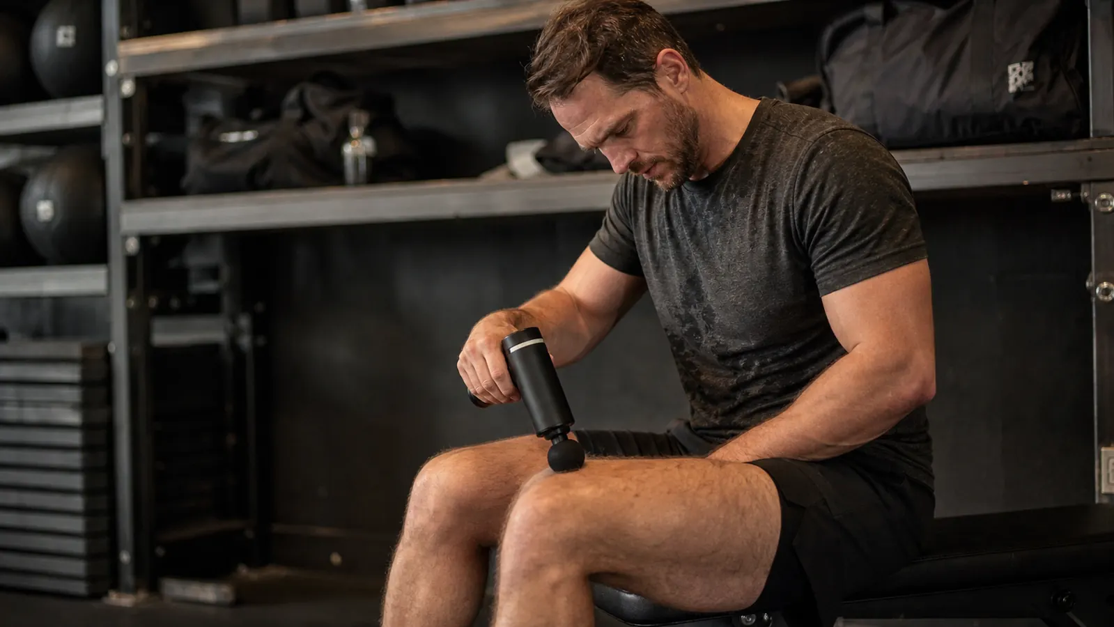 Person using the Theragun Relief massage gun on their quad after a workout, gym bag and water bottle in the background